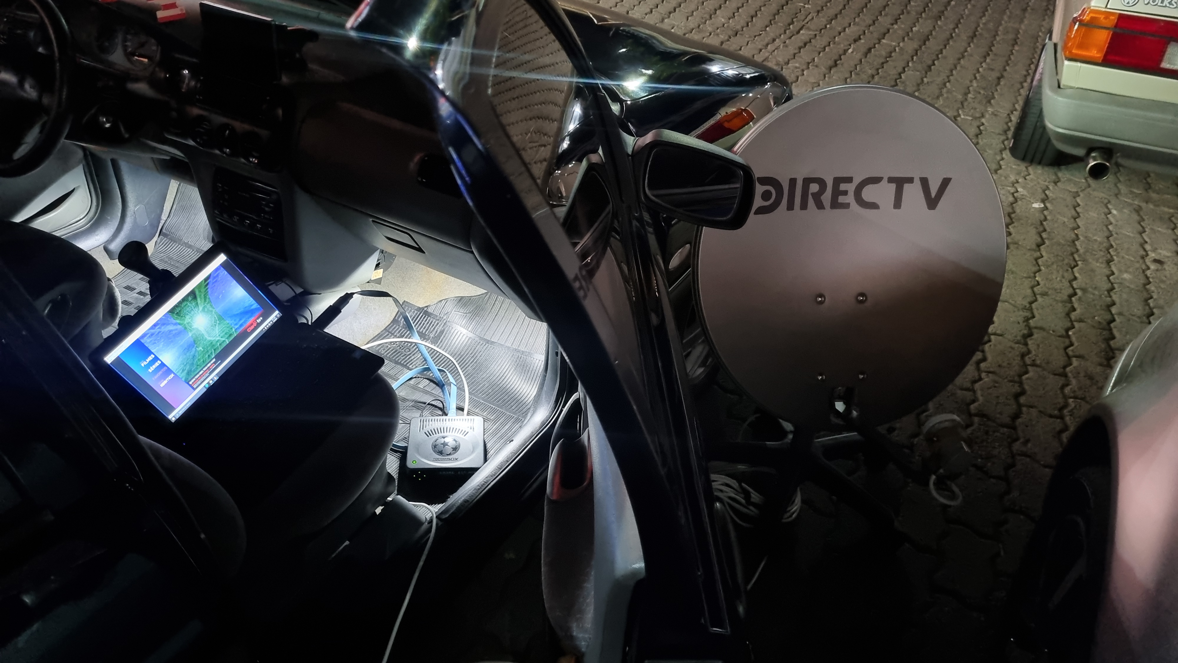 O cenário da gambiarra perfeita: receptor alimentado pela tomada 12v do carro, antena apontada para satélite no meio de um posto de gasolina e o laptop exibindo a imagem do sinal capturado